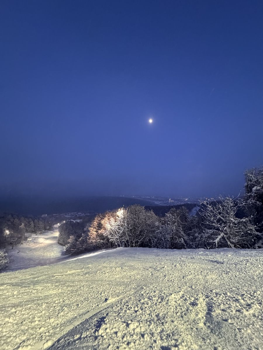黃昏月亮升起時亮起照明的 Onze 雪道,遠處是海
