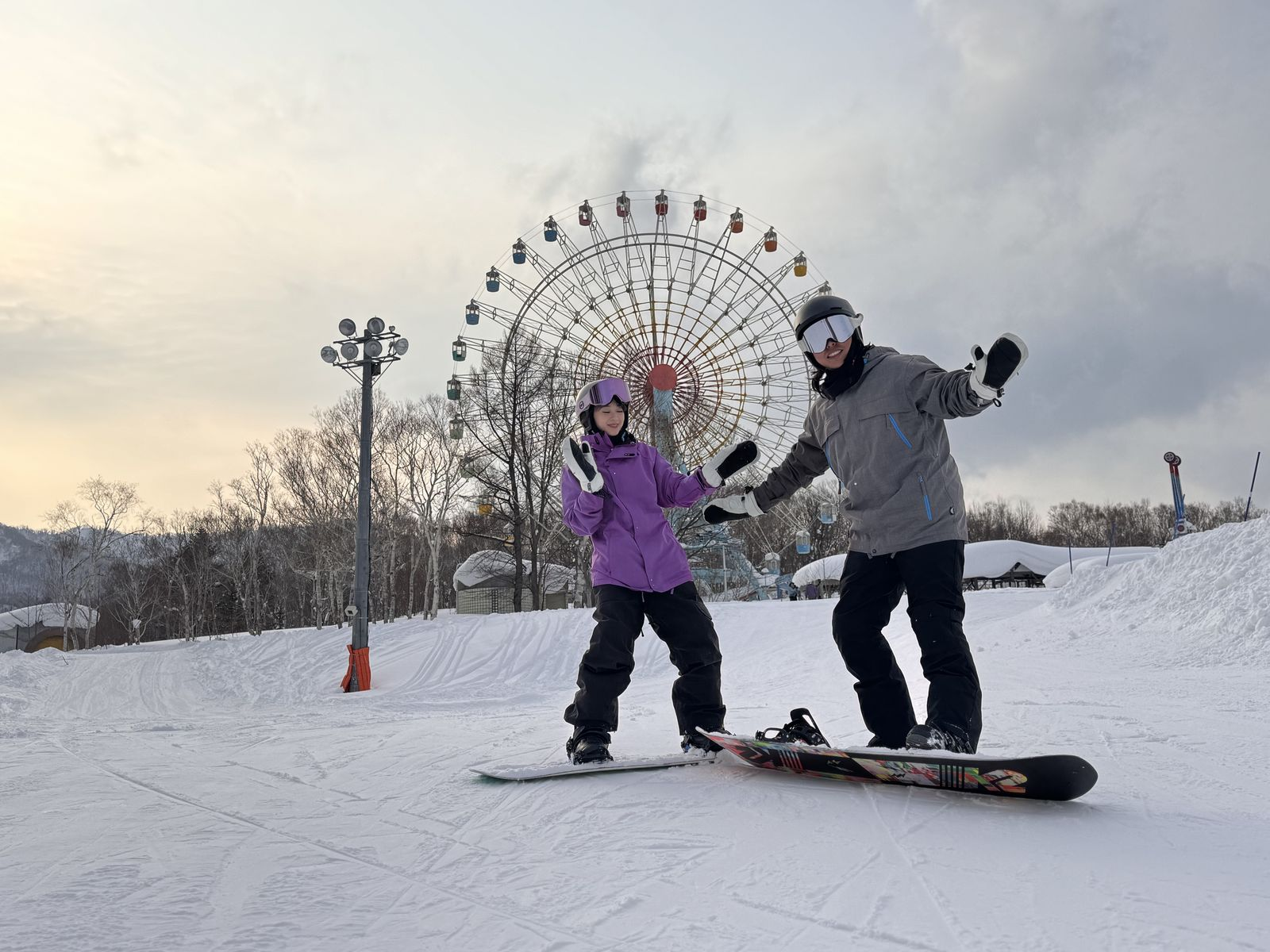 兩位單板學員在手稻 Olympia 區雪道上揮手，背後是大觀覽車